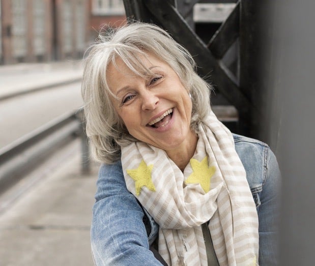 Grauhaarige, lachende, glückliche Frau in Jeansjacke mit Schal