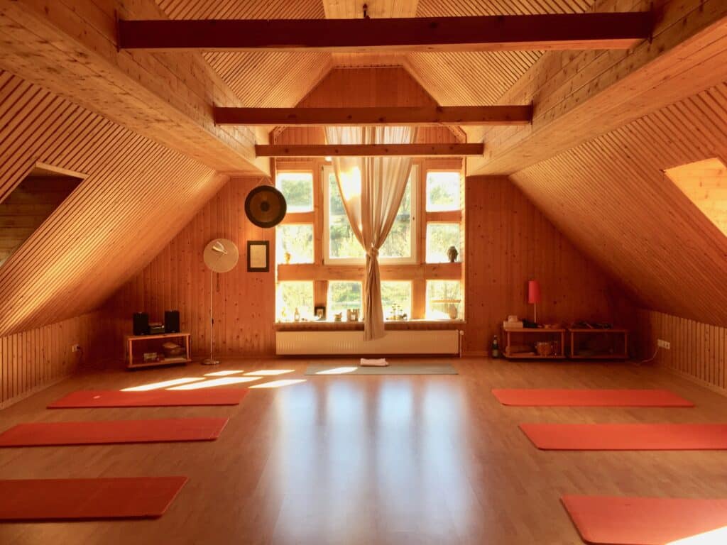 Yogaraum in Holz gehalten und von Sonnenlicht durchflutet mit orangenen Yogamatten