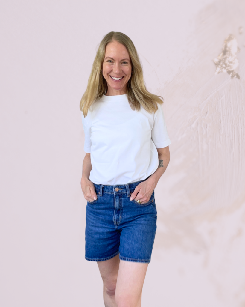 Blonde lächelnde Frau in weißem T-Shirt und Jeansshorts